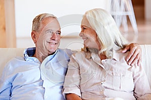 Senior white couple relaxing at home, looking at each other smiling, front view, close up
