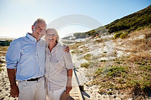 Senior white couple standing on a beach embracing and smiling to camera, three quarter length photo
