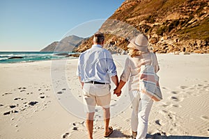 Senior white couple walking on a beach holding hands, back view, three quarter length, close up photo