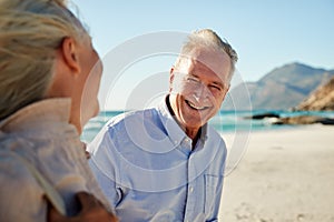 Senior white couple walking on a beach, looking at each other and smiling, waist up, close up