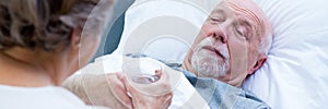 Senior wife giving glass of water to her sick husband