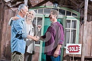 Senior wife holding keys of new house while her husband shaking hands with saleman photo