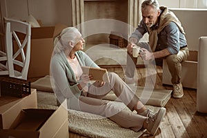 Senior wife showing old photo to her husband while taking break from packing cardboard boxes