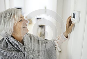 Senior woman adjusting her thermostat at home