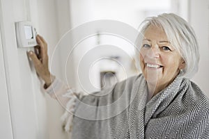 Senior woman adjusting her thermostat at home