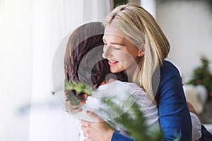 Senior woman with adult daughter at home at Christmas time, hugging.