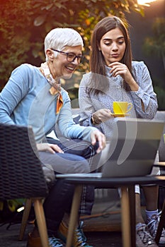 Senior woman and adult girl sitting outdoors at home and enjoying at coffee