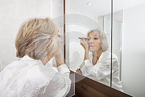 Senior woman applying eyeliner while looking at mirror in bathroom