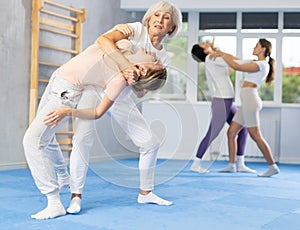 Senior woman applying inverted headlock during mock bout in self-defense training