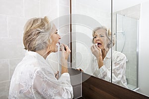 Senior woman applying lipstick while looking at mirror in bathroom