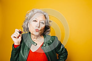 Senior woman applying red lipstick over a yellow background