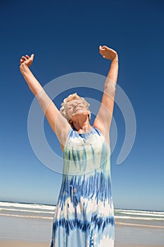 Senior woman with arms raised standing against clear sky