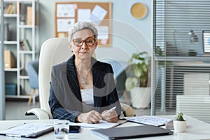 Senior woman as female boss sitting at workplace in office and looking at camera