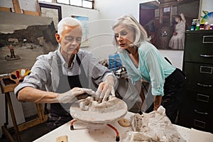 Senior woman assisting senior man in making pottery during drawing class