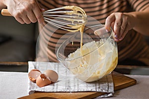 Senior woman beats eggs with flour for dough with a wisk in a glass bowl. Ingredients for a christmas pie or pancakes.