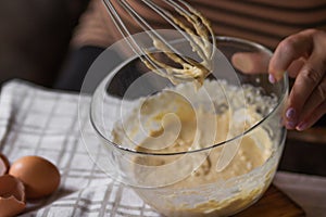 Senior woman beats eggs with flour for dough with a wisk in a glass bowl. Ingredients for a christmas pie or pancakes.