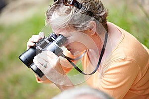 Senior, woman and binocular in forest for travel, sightseeing or vacation and scenery in nature. Elderly, lady or person