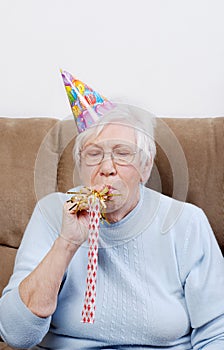 Senior Woman With Birthday Hat Blowing Noise Maker