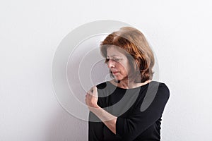 Senior woman in black t-shirt, studio shot against white wall.