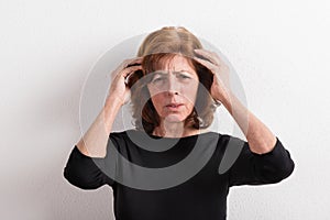 Senior woman in black t-shirt, studio shot against white wall.