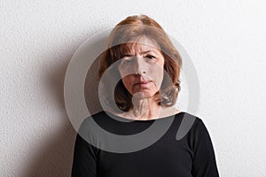 Senior woman in black t-shirt, studio shot against white wall.