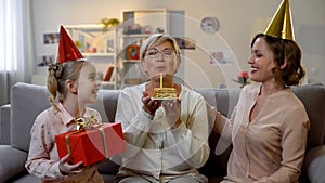 Senior woman blowing candle on cake, family congratulating granny, celebration