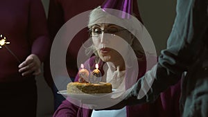 Senior woman blowing out candles on cake and smiling, celebrating 80 birthday