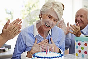 Senior Woman Blows Out Birthday Cake Candles At Family Party