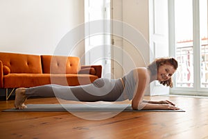 Senior woman with bright smile maintaining plank pose while training at home