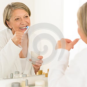 Senior woman brushing teeth bathroom mirror