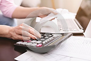 Senior woman calculating taxes at home, using calculator