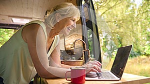 Senior Woman On Camping Trip In Countryside Working Inside RV Using Laptop