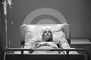 Senior woman with cancer lying alone in hospital bed during chemotherapy, black and white photo