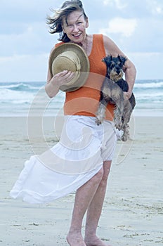 Senior woman carrying pet puppy dog on the beach for day out photo