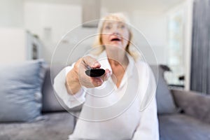 Senior woman changing channel with remote control at home