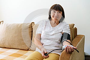 Senior woman checking blood pressure level at home, elderly woman suffering