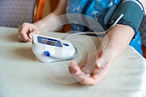 Senior woman checking blood pressure level at home, older female suffering from high blood pressure, sitting and using a