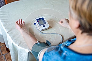 Senior woman checking blood pressure level at home, older female suffering from high blood pressure, sitting and using a