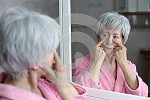 Senior woman checking her puffy eyes out