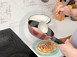 Senior woman chef pour portion of liquid dough by hands with ladle on frying pan for baking delicious pancakes, crepes