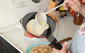 Senior woman chef pour portion of liquid dough by hands with ladle on frying pan for baking delicious pancakes, crepes