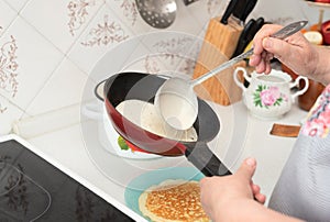 Senior woman chef pour portion of liquid dough by hands with ladle on frying pan for baking delicious pancakes, crepes