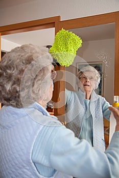 Senior woman cleaning mirror at home