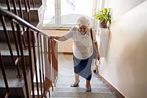 Senior woman climbing staircase with difficulty