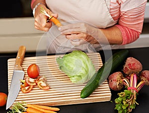 Senior woman or closeup with salad in kitchen and cutting, tomato and carrots for diet. Female chef and zoom with