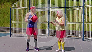 Senior woman coach teaching grandfather with basketball dribbling exercise with ball on playground