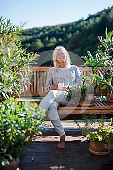 Senior woman with coffee sitting outdoors on terrace, resting.