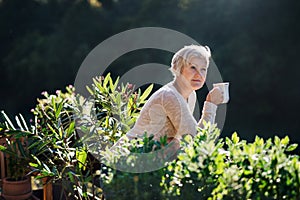 Senior woman with coffee standing outdoors on terrace, resting.