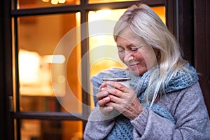 Senior woman with coffee standing outdoors on terrace, resting.