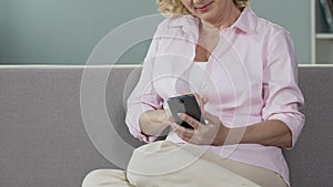 Senior woman on couch looking at mobile phone, scrolling screen, past memories